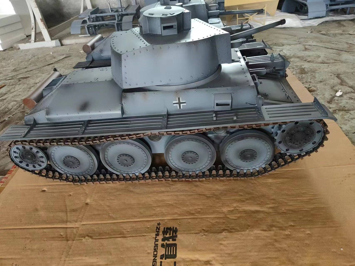 A detailed eaxtoys 1/6 scale Panzerkampfwagen 38(t) model in grey rests on cardboard, displaying a distinct turret, tracks, and a small cross emblem. Tools and materials are scattered around—a real treasure for military model enthusiasts.
